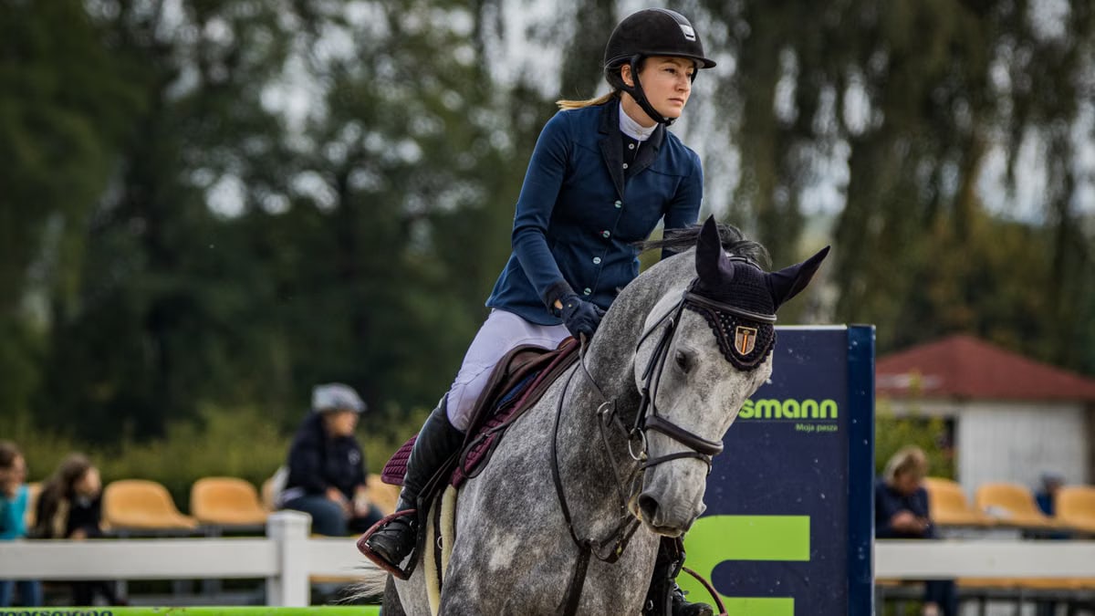 A female equestrian riding a gray horse during a competition, showcasing skill and focus.